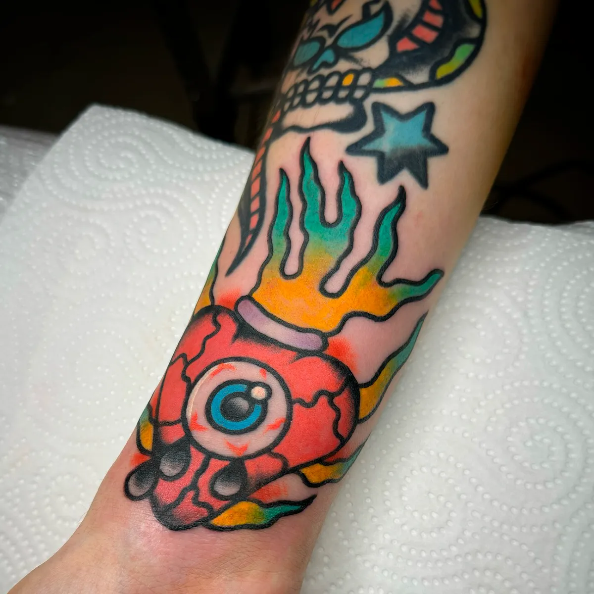 Tatuaje de ojo con llamas de colores en el antebrazo